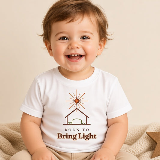Smiling toddler in the Born to Bring Light star and stable Christmas tee