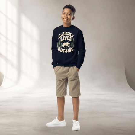 Boy standing in a studio wearing a navy crewneck sweatshirt with 'Curiosity Lives Outside' woodland artwork