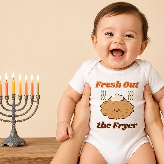 Laughing baby in the Fresh Out the Fryer Hanukkah bodysuit beside a menorah