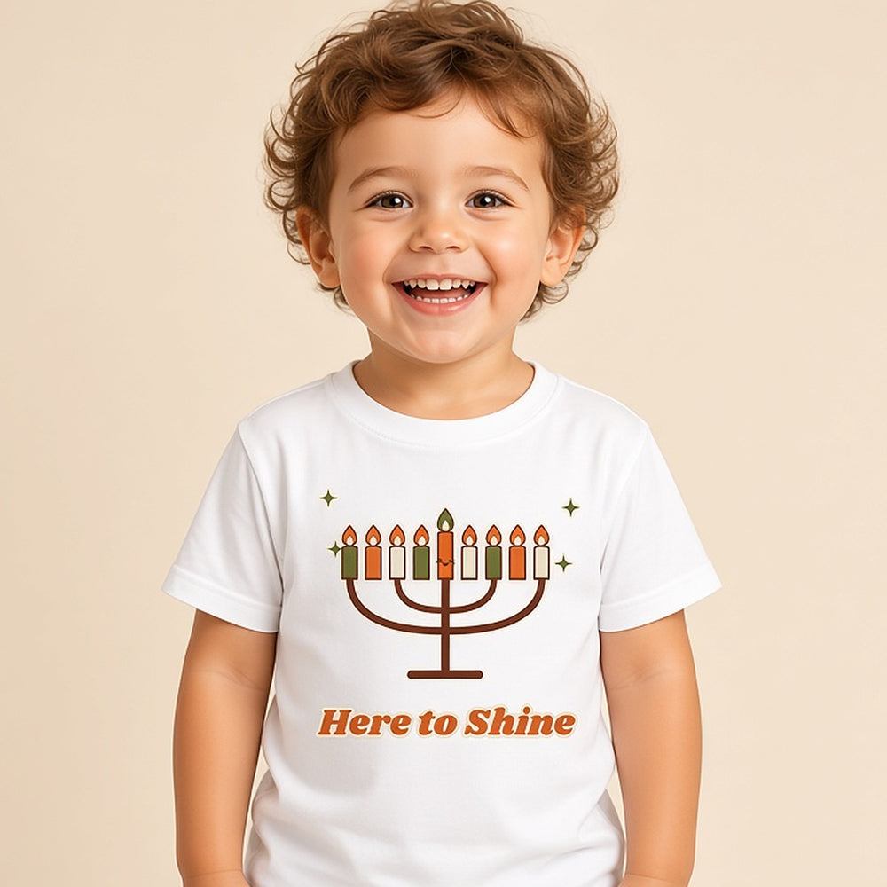 Toddler in the white Here to Shine menorah Hanukkah tee