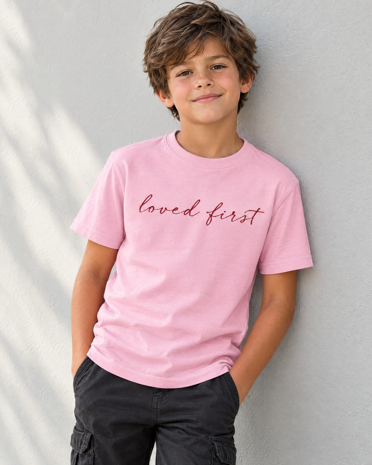 Kid wearing the Pink Loved First Kids Christian Tee – 'We Love Because He First Loved Us' Pink Graphic Tee - lifestyle photo, Cartsy