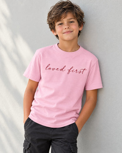 Kid wearing the Pink Loved First Kids Christian Tee – 'We Love Because He First Loved Us' Pink Graphic Tee - lifestyle photo, Cartsy