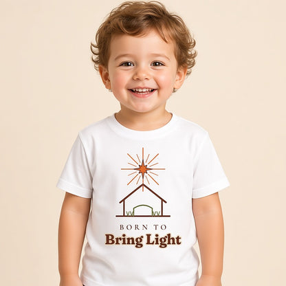 Toddler in a white Born to Bring Light Christmas tee with a star over a stable