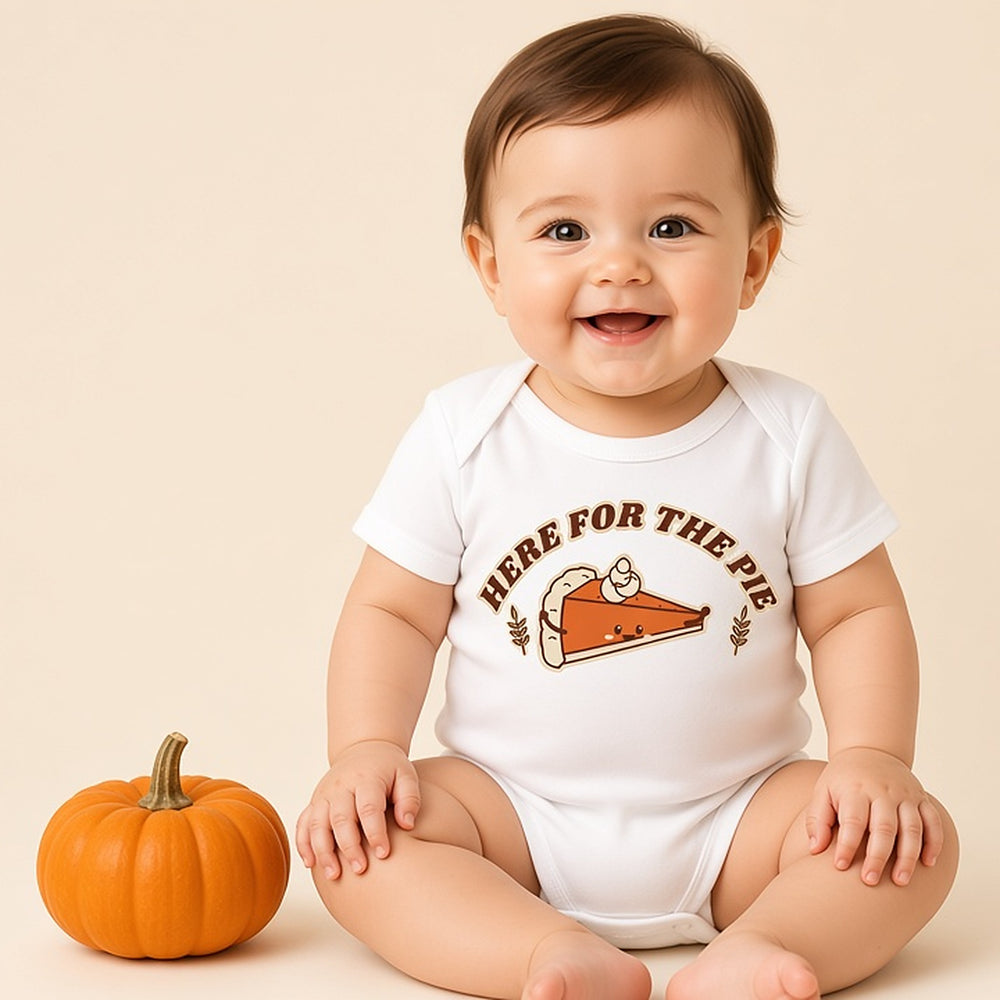Smiling baby sitting in the white Here for the Pie first Thanksgiving bodysuit beside a mini pumpkin