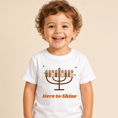 Toddler in the white Here to Shine menorah Hanukkah tee