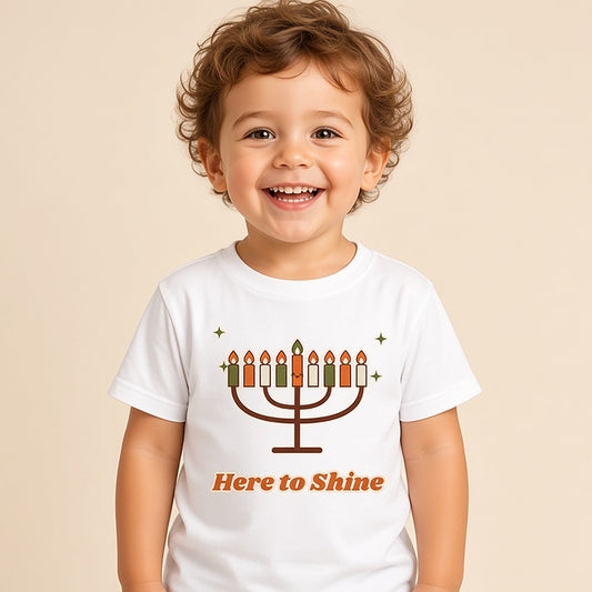 Toddler in the white Here to Shine menorah Hanukkah tee