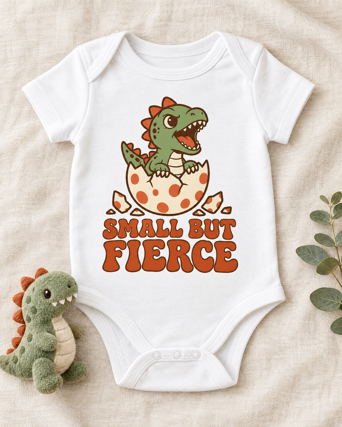 Flat lay of the Small But Fierce baby bodysuit with a plush dinosaur