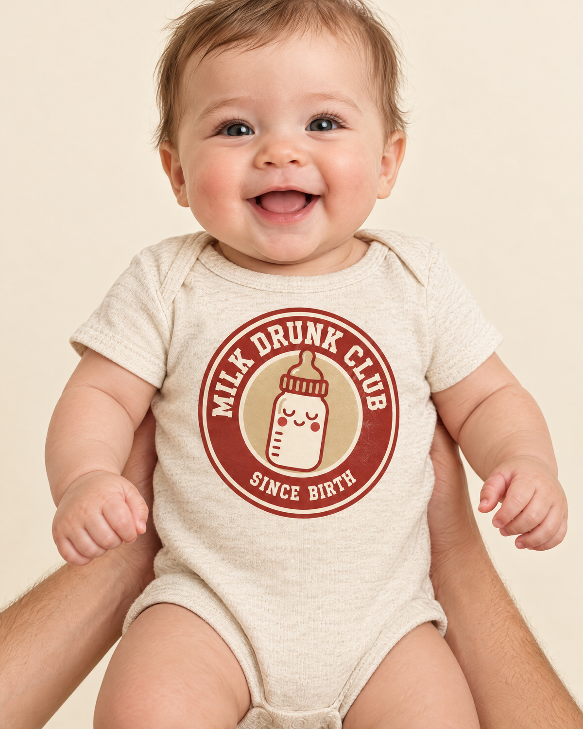 Smiling baby held by a parent wearing the Milk Drunk Club bodysuit