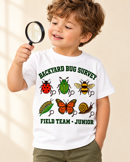 Curious toddler holding a magnifying glass in the Backyard Bug Survey t-shirt