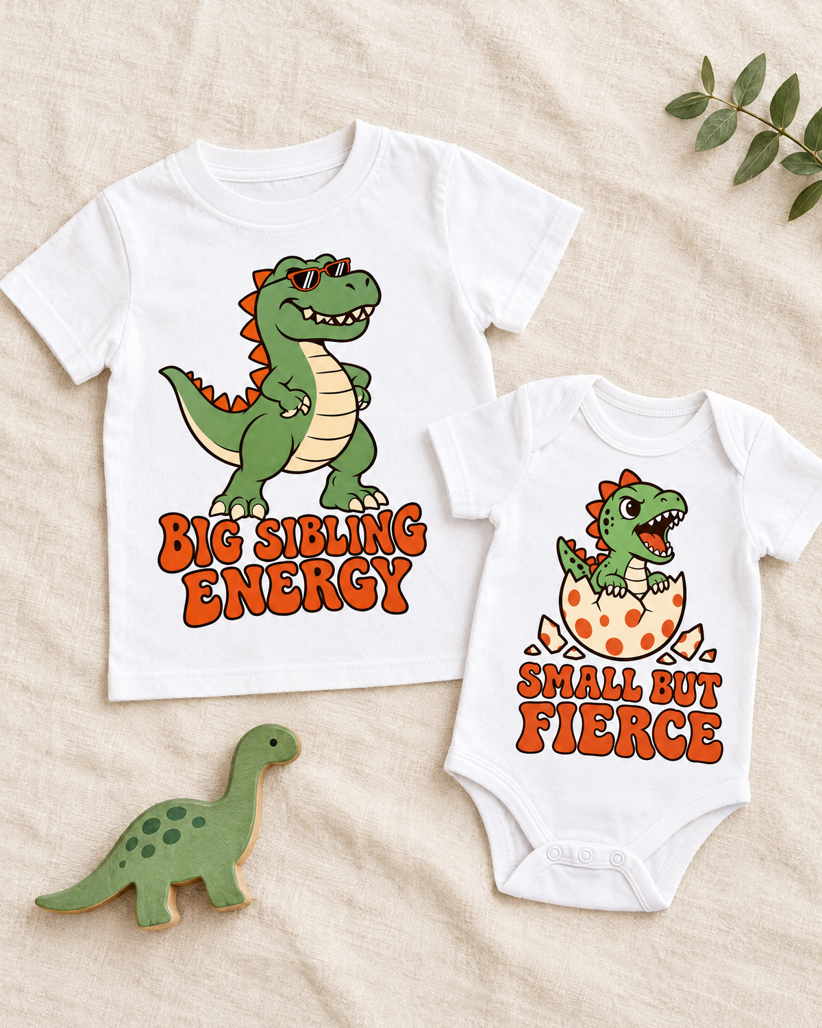 Flat lay of matching Big Sibling Energy tee and Small But Fierce bodysuit with toy dinosaur