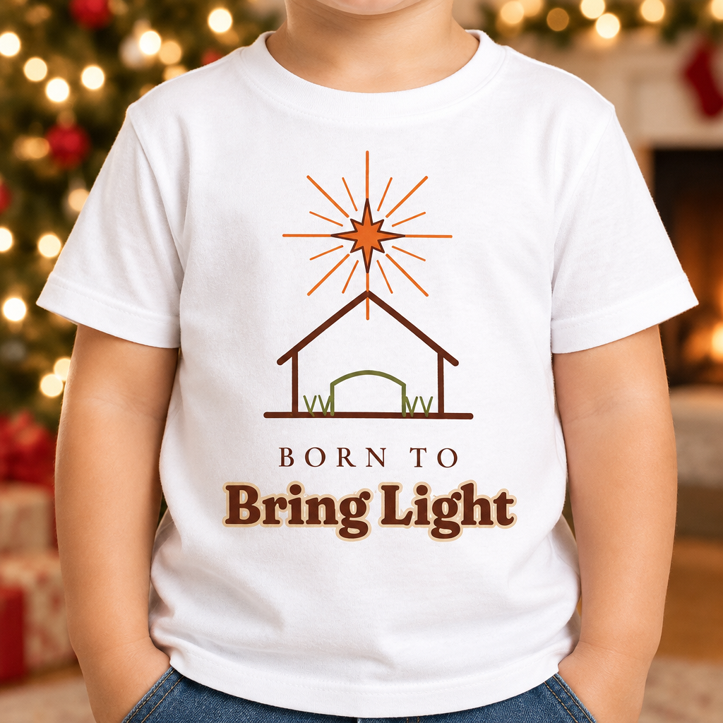 Child wearing the Born to Bring Light Toddler Christmas Shirt: Faith Tee in a cozy Christmas living room, cropped torso view