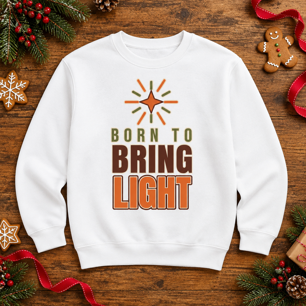Flat lay of the Modern Christian Kids Sweatshirt: Born to Bring Light Bold on a wooden table with pine sprigs and gingerbread cookies