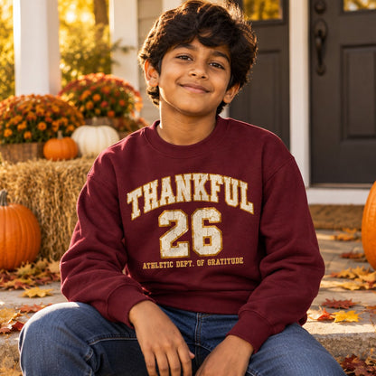 Kid wearing the Maroon Thankful Varsity kids Thanksgiving crewneck sweatshirt with a gold and cream varsity print