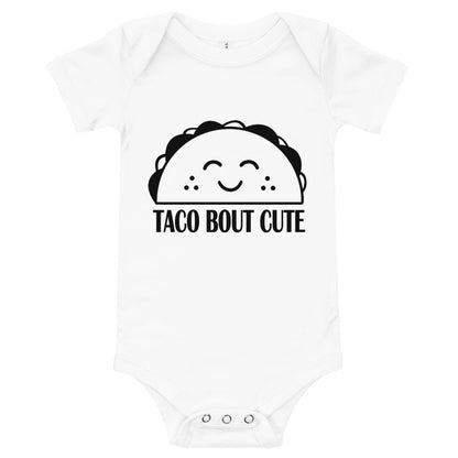 White baby bodysuit with a smiling cartoon taco and the words 'Taco Bout Cute'